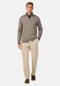 Moška svetlo siva zip-up jopica z rebrastimi manšetami in robom. V kombinaciji s svetlo bež hlačami in rjavimi čevlji. Preprost, prilegajoč se dizajn.