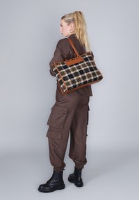 Kabelka s černobílým károvaným vzorem a hnědými koženými uchy, obdélníkový tvar s texturovanou látkou, spárovaná s hnědými cargo kalhotami a černými botami.