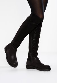Stivali neri sopra il ginocchio in una combinazione di suede liscio e testurizzato. Presentano una suola chunky bassa e una zip laterale per facilitare l'indossamento.