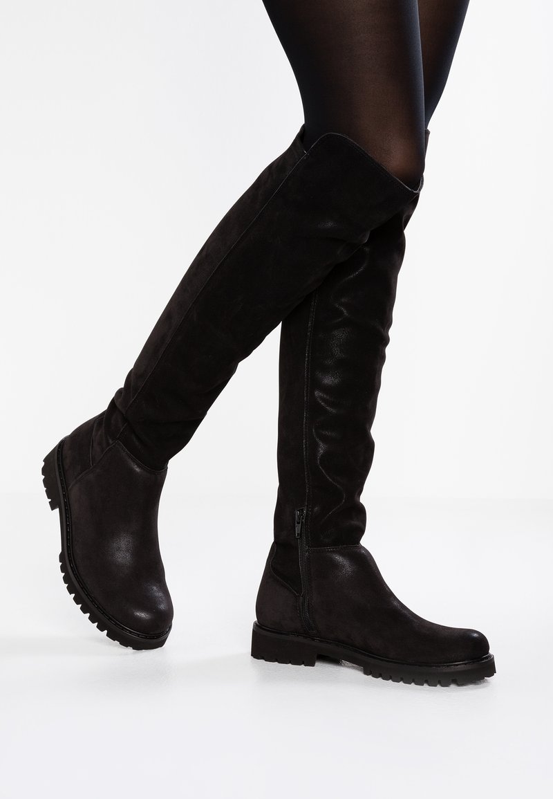 Stivali neri sopra il ginocchio in una combinazione di suede liscio e testurizzato. Presentano una suola chunky bassa e una zip laterale per facilitare l'indossamento.