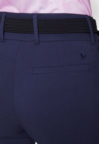 Marineblaue Hose mit einem strukturierten schwarzen gewebten Gürtel, ausgestattet mit einer Gesäßtasche und dezenter Markenkennzeichnung. Glattes Material mit maßgeschneidertem Schnitt.