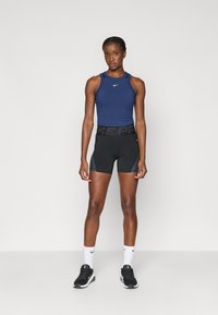 Σπορ crop top σε ναυτικό χρώμα με το λογότυπο της Nike, συνδυασμένο με μαύρα κολάν συμπίεσης με φαρδύ μαύρο λάστιχο στη μέση. Λευκές κάλτσες και μαύρα αθλητικά παπούτσια.