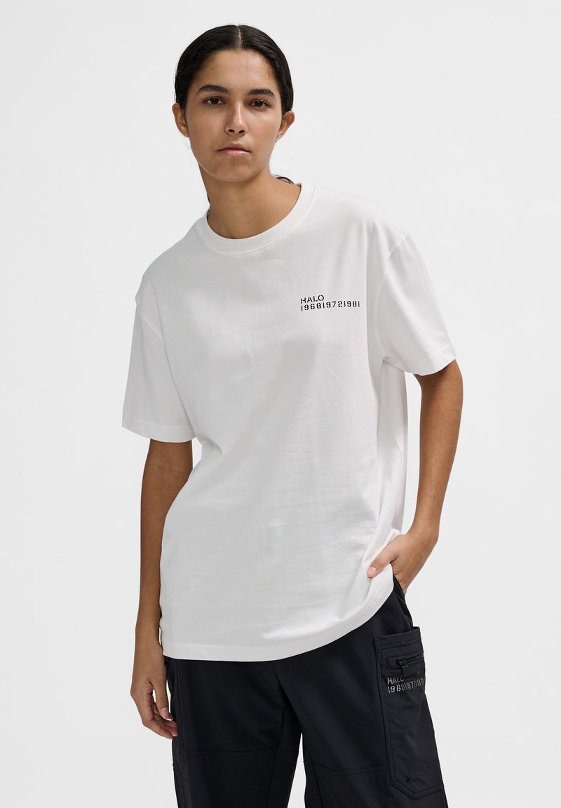 Biała oversize'owa koszulka z bawełny, z nadrukowanym czarnym napisem na lewej piersi. Okrągły dekolt i krótkie rękawy.