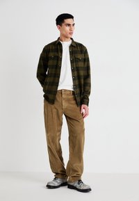 Grønn og svart rutete flanellskjorte over en hvit t-skjorte, sammen med beige kordfløyelsbukser og grå snørestøvler.