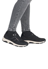 Schwarze Wildledersneaker mit glatter Textur, ausgestattet mit einem Reißverschlussdetail, weißer Sohle und schwarzen Akzenten. Entwickelt für Komfort und Unterstützung.