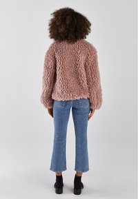 Luddig, ljusrosa jacka med en texturerad, plyschyta; kombinerad med blå utsvängda jeans och svarta ankelboots. Bakre vy av outfiten.