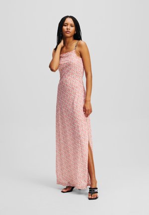 Maxi dress in pink with geometric pattern, featuring a straight neckline, thin straps, and a side slit, paired with black flat sandals.