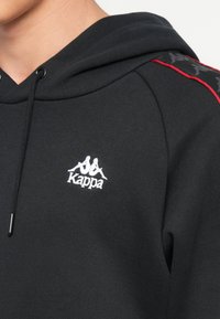 Sudadera Kappa negra con logo frontal, que incluye capucha con cordón, puños acanalados y acentos laterales rojos con un diseño estampado.