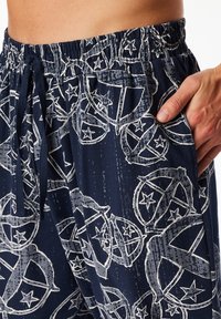Marineblaue Hose mit elastischem Bund und Kordelzug. Sie verfügt über ein Design mit weißen Sternen und kreisförmigen Motiven. Inklusive seitlicher Taschen.