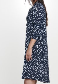 Abito navy con pois bianchi, caratterizzato da maniche lunghe, un colletto arricciato e un taglio morbido che arriva sopra il ginocchio.