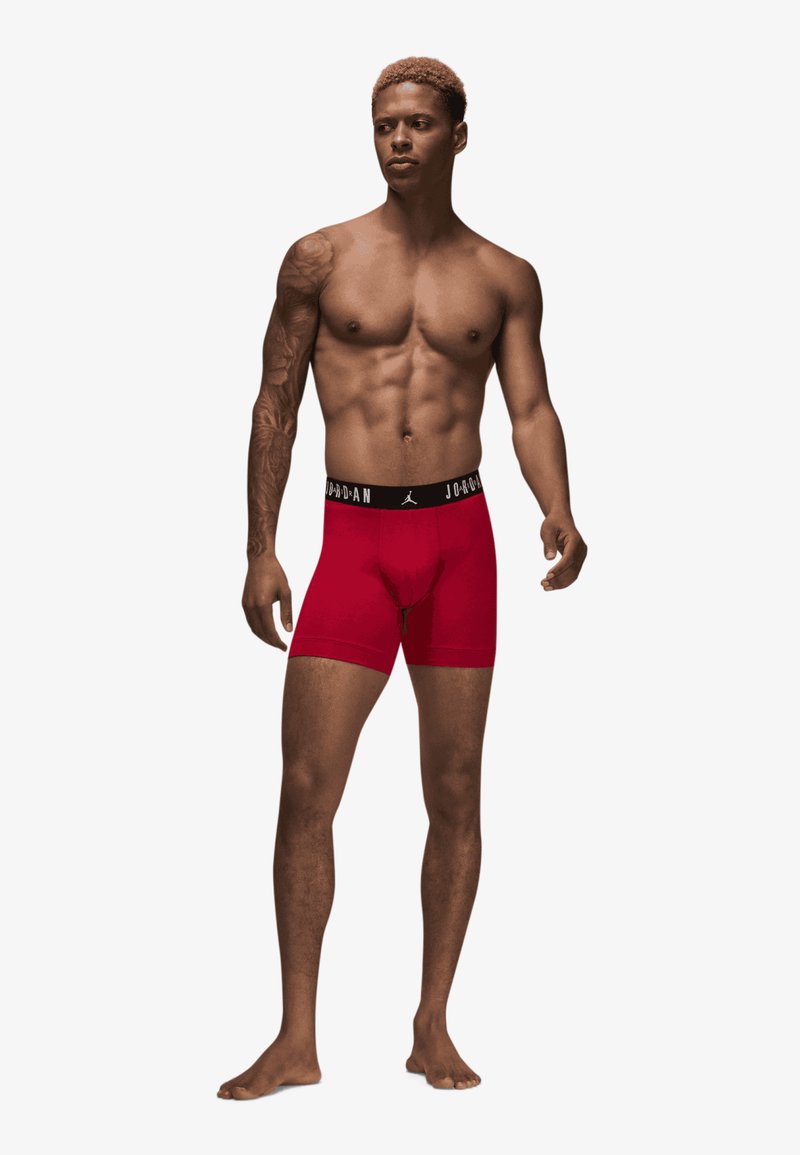 Røde tætsiddende boxer briefs med en sort elastik, der har "JORDAN" branding. Lavet af strækbart materiale, designet til komfort og støtte.