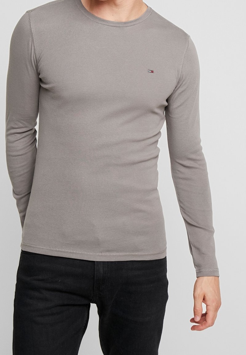 Graues langärmliges T-Shirt aus Baumwollmischung mit Rundhalsausschnitt; verfügt über ein minimales Logo auf der Brust, eine glatte Textur und eine figurnahe Passform.