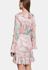 Abito a manica corta con cappuccio in rosa pastello, decorato con motivi astratti in turchese e bianco, con un orlo a balze a strati e una vita con cintura.