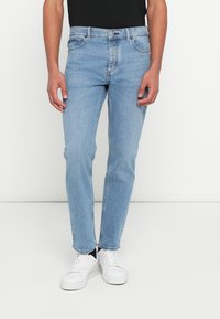 Jasnoniebieskie jeansy z denimu o prostym kroju, z zapięciem na suwak, pięcioma kieszeniami i subtelnym przetarciem, zestawione z białymi trampkami.