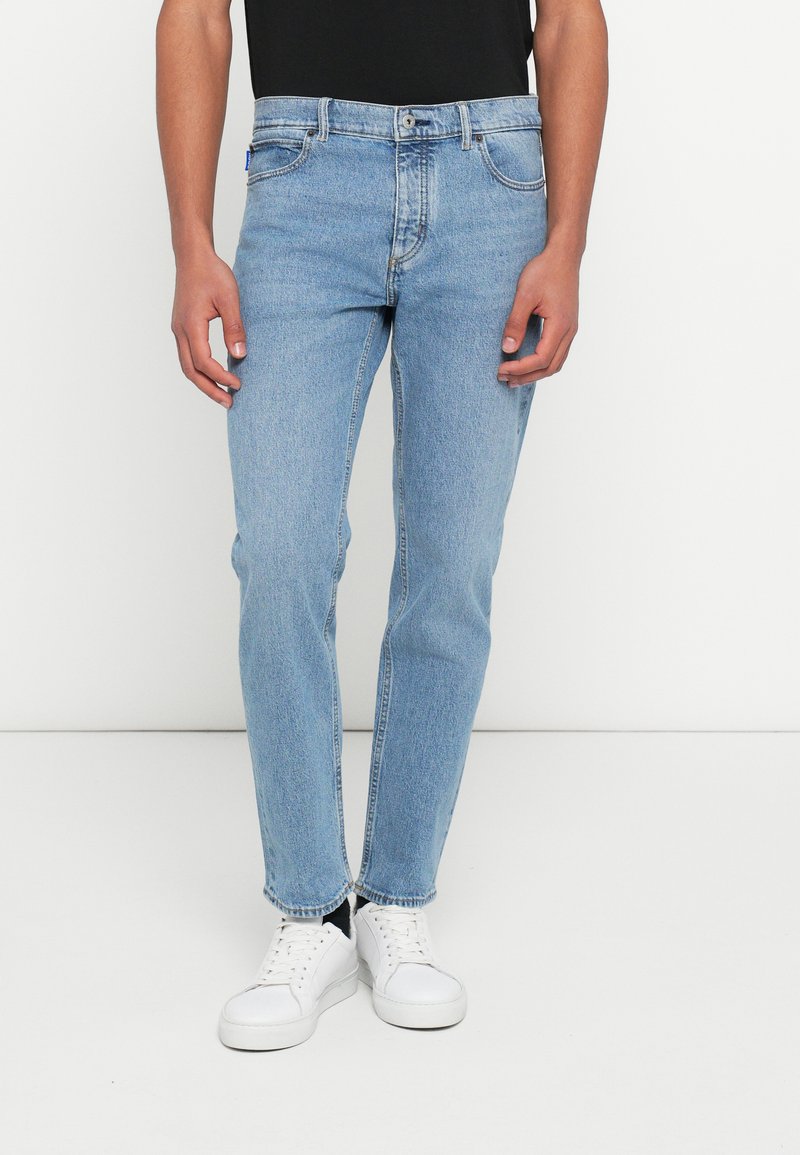 Jasnoniebieskie jeansy z denimu o prostym kroju, z zapięciem na suwak, pięcioma kieszeniami i subtelnym przetarciem, zestawione z białymi trampkami.