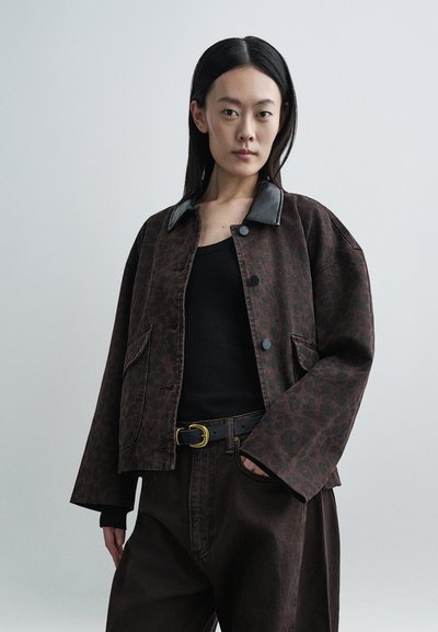 Veste imprimé léopard marron avec col noir, ornée de grands boutons et deux poches avant. Portée sur un haut noir côtelé et un pantalon marron.