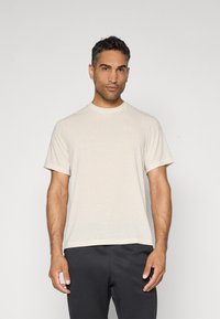 Camiseta de manga corta beige hecha de tejido suave, con cuello redondo y un sutil logo blanco de Nike en el lado izquierdo del pecho.