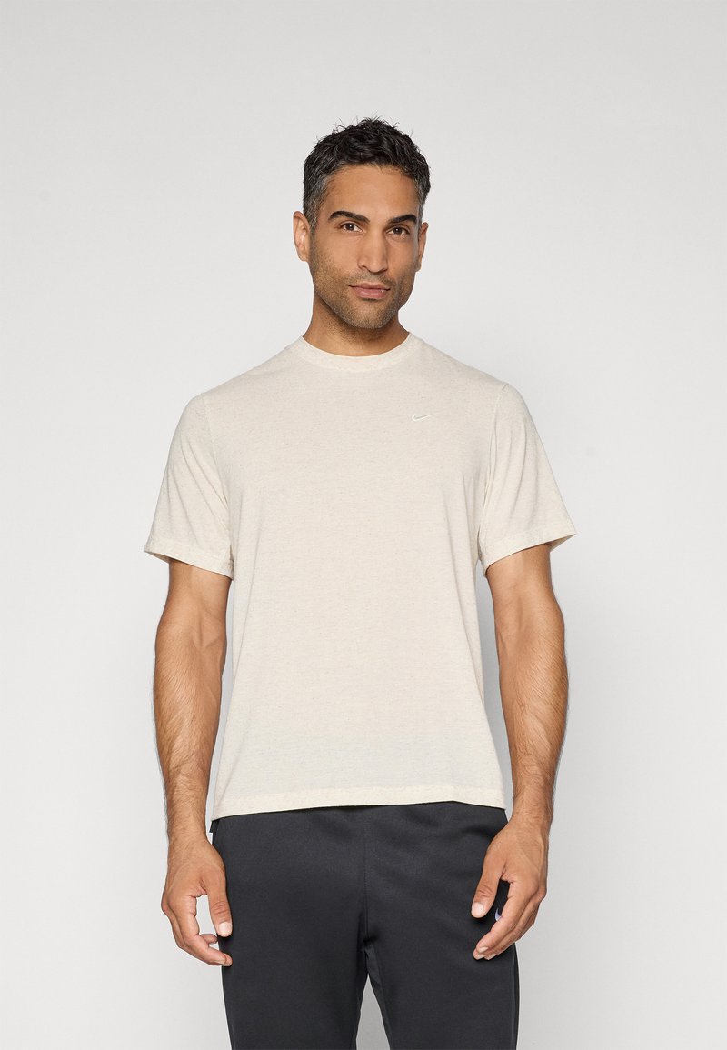 Camiseta de manga corta beige hecha de tejido suave, con cuello redondo y un sutil logo blanco de Nike en el lado izquierdo del pecho.