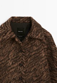 Manteau boutonné marron à texture duveteuse avec col large, étiqueté Massimo Dutti, fabriqué au Portugal, présenté sur fond blanc.