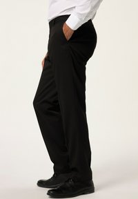Pantaloni neri a vestibilità slim, con un design a vita piatta, tasche laterali e texture liscia, abbinati a scarpe eleganti nere.