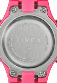 Élément arrière de montre Timex en acier inoxydable, avec texte gravé. Accents en plastique rose vif sur les côtés et vis métalliques sécurisées visibles.