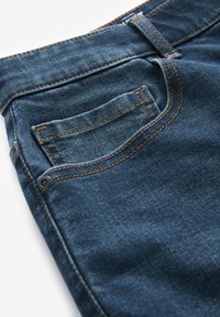 Dunkelblaue Denim-Jeans mit einer Gesäßtasche, kontrastierenden orangen Nähten und einer subtilen Textur mit glatter Oberfläche.