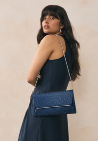 Navy blue clutch bag with textured surface, adorned with small, shiny details. Features a silver chain strap and rectangular shape.