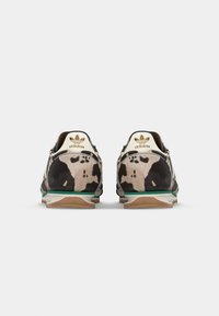 Adidas sneakers with a patterned black and beige upper, green accents, and a white sole. Features logo at the heel and textured material.