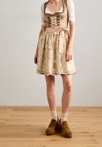 Traditional dress with a lace top, beige bodice, and embroidered skirt. Features a ribbon belt and layered lace hem. Brown platform shoes.