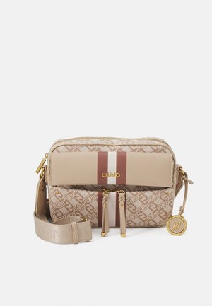 Beige og brun mønstret crossbody taske med forreste lynlåslommer, justerbar rem, gyldne detaljer og en rund logo vedhæng hængende på siden.