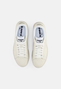 Baskets en cuir blanc avec des lacets blancs, bout perforé et branding sur la languette et la semelle intérieure. Texture lisse et design minimaliste.