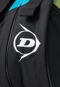 Schwarze Stofftasche mit einer strukturierten Oberfläche. Verfügt über ein auffälliges weißes Logo in einem kreisförmigen Design und einen türkisfarbenen Akzent entlang der Oberseite.