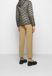 Veste matelassée noire et beige avec capuche, associée à un pantalon beige fuselé et des chaussures noires épaisses. Motif en chevrons visible sur la veste.