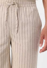 Lyse beige linned bukser med lodrette marineblå striber, der har en elastisk talje og snørrebånd. Indeholder sidelommer og en afslappet pasform.
