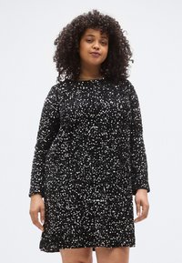 Fekete ruha flitterekkel borítva, hosszú ujjú, kerek nyakkivágással, enyhén bővülő szoknyával. Az anyag fényes, texturált megjelenésű, tükröződő részletekkel.