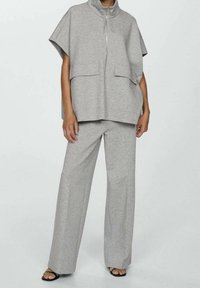 Pull en gris court avec col haut et deux poches avant, associé à un pantalon large gris. Fabriqué en tissu doux et léger.