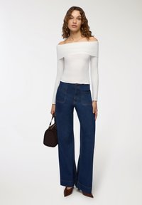 Biała, prążkowana bluzka bez ramiączek zestawiona z niebieskimi dżinsami o wysokim stanem i szerokich nogawkach. Brązowa torebka i brązowe szpilki dopełniają całość.