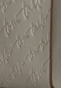 Bolso de mano metálico beige con un diseño en relieve que presenta el texto "tom tailor". Textura suave y detalle de borde marrón contrastante.