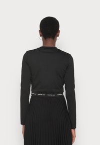 Camiseta negra de manga larga con un diseño ajustado, que presenta un corte cropped y una banda en la cintura con "Calvin Klein Jeans" en texto blanco.