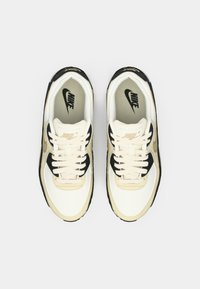 Nike spordijalatsid on beez ja valge pealispind mustade detailidega, tekstuuriga nahk, ümmargused paelad ja pehme sisetald logoga.