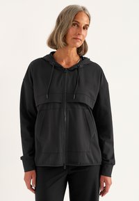 Zwarte zip-up hoodie met een voorzak, trekkoordcapuchon en een soepele textuur. Bevat een horizontale naad over de borst.