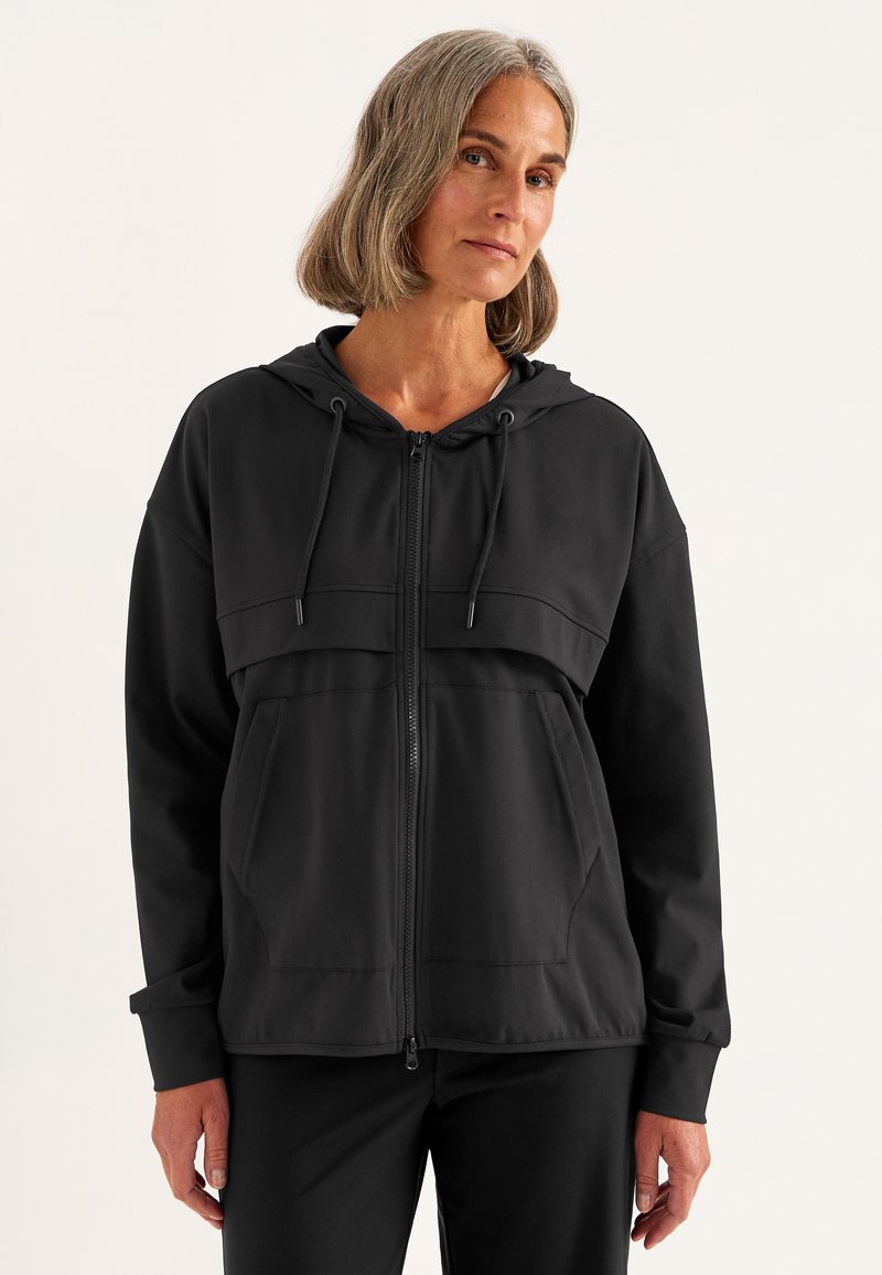Zwarte zip-up hoodie met een voorzak, trekkoordcapuchon en een soepele textuur. Bevat een horizontale naad over de borst.