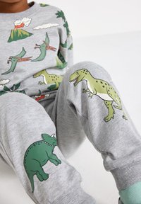 Gray cotton sweatshirt and sweatpants feature colorful dinosaur and volcanic prints. The fabric is soft, with ribbed cuffs and various designs.