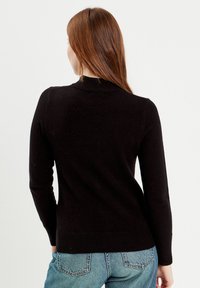 Sort sweater med en tætsiddende design og ribbet halsudskæring. Lange ærmer og en lidt længere bagkant. Bæres med lyseblå jeans.