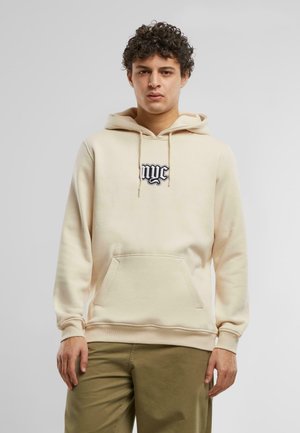 Béžová mikina vyrobená z mäkkej tkaniny, s klokankou, so sťahovacími šnúrkami a čiernym logom "nyc" v štýlovom písmene na hrudi.