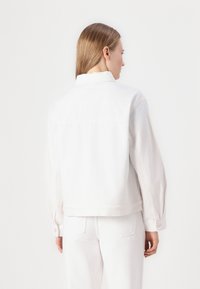 Bela denim jakna z ohlapnim krojem, gumbi na manšetah in ravnim robom. Ima klasičen ovratnik in minimalističen dizajn.