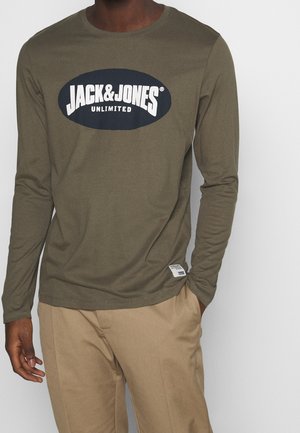 Camisa de manga larga de color verde oliva con cuello redondo, que presenta un gran logo ovalado azul marino con la inscripción "JACK & JONES UNLIMITED". Detalle de etiqueta lateral visible.