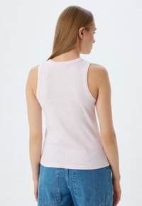 Hellrosa gerippte Tanktop mit Rundhalsausschnitt und schmalen Trägern, kombiniert mit blauen Denim-Shorts, die eine lockere Passform und glatte Textur zeigen.