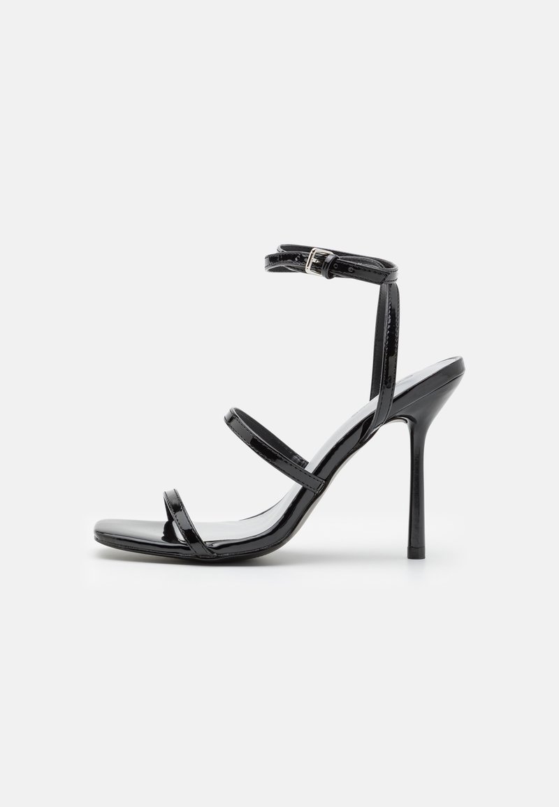 Sandale à talon haut en cuir verni noir avec fines bandes sur les orteils, le médio-pied et fermeture à boucle à la cheville, présentée sur fond blanc.