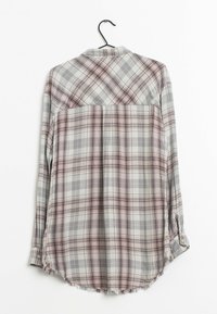 Plaid shirt in gray, pink, and white. Long sleeves, a curved hem, and a frayed bottom edge. Made of a soft fabric with a checkered pattern.
